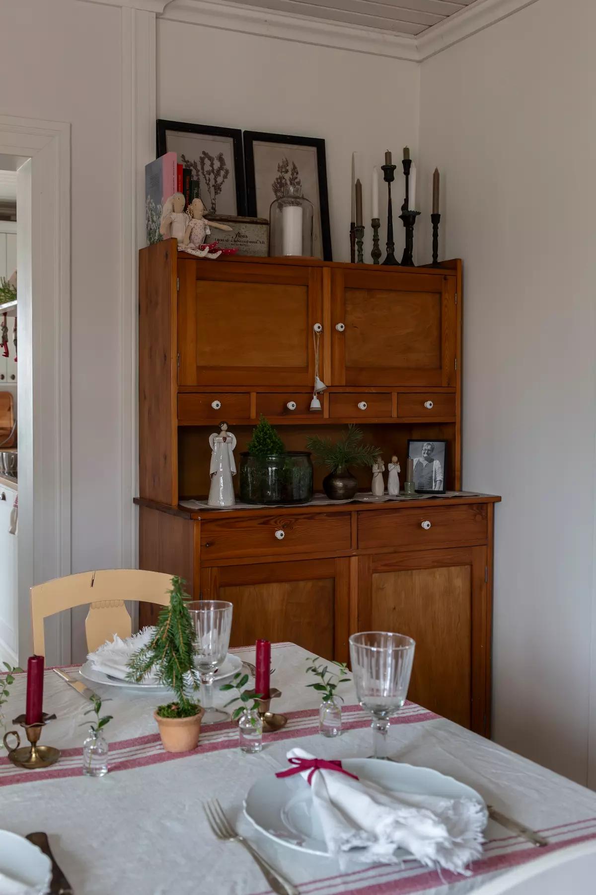 Table with a small Christmas tree, candles and tableware against a wooden buffet