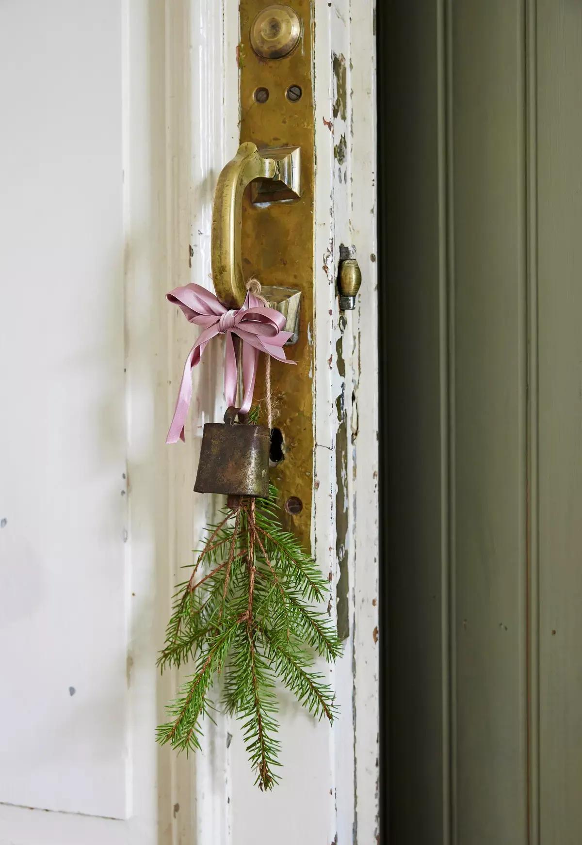 Door handle decorated with a pink ribbon, a rusty bell and a sprig of fir