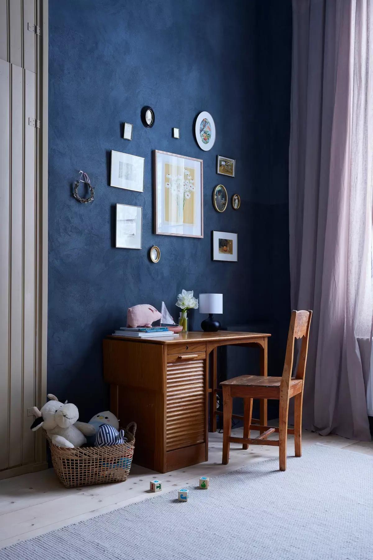 Child’s room with a dark-blue wall, wooden desk and chair, framed pictures and a toy basket