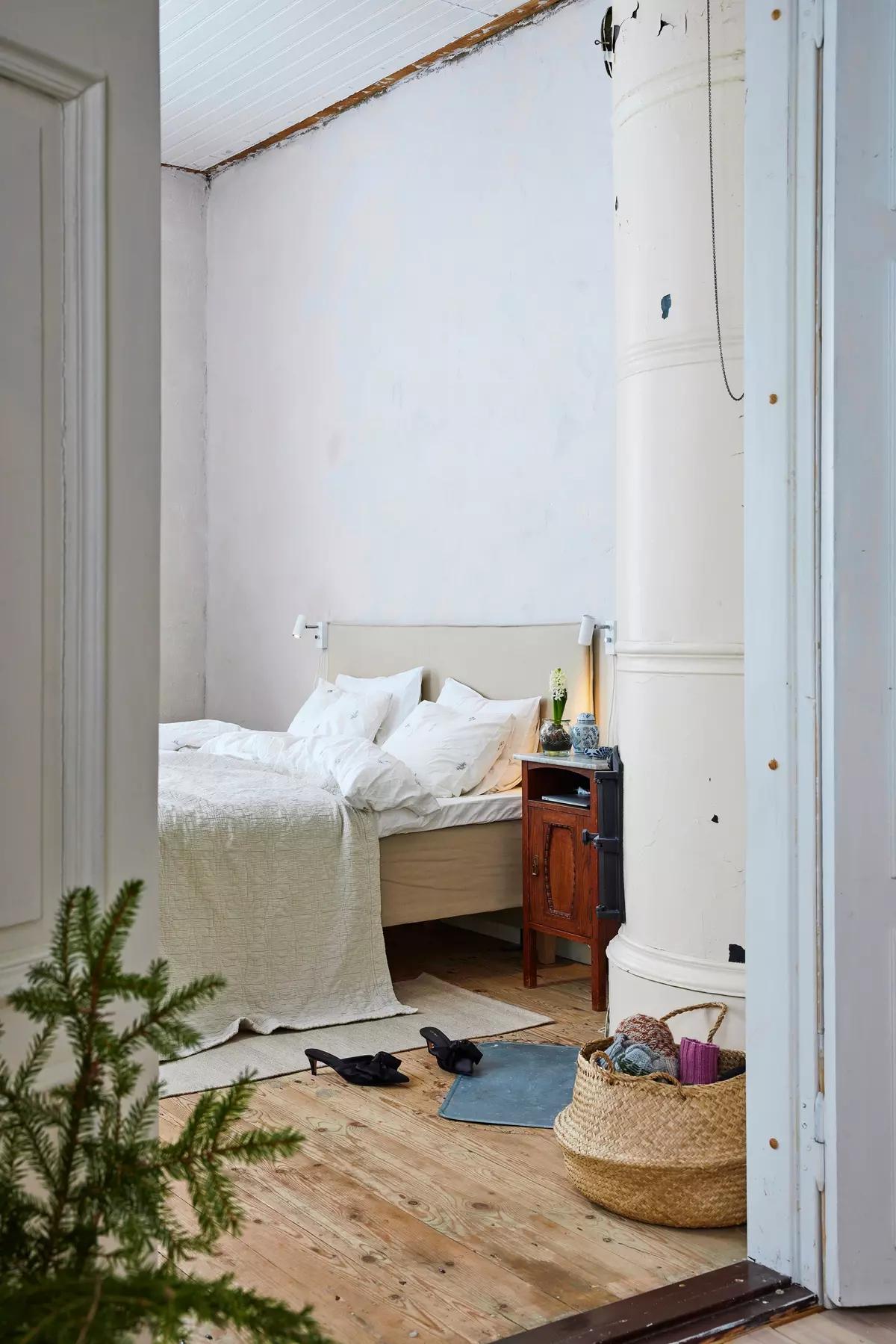 Bedroom with a bed, vintage nightstand, white stove, a basket of yarn, shoes and a small Christmas tree