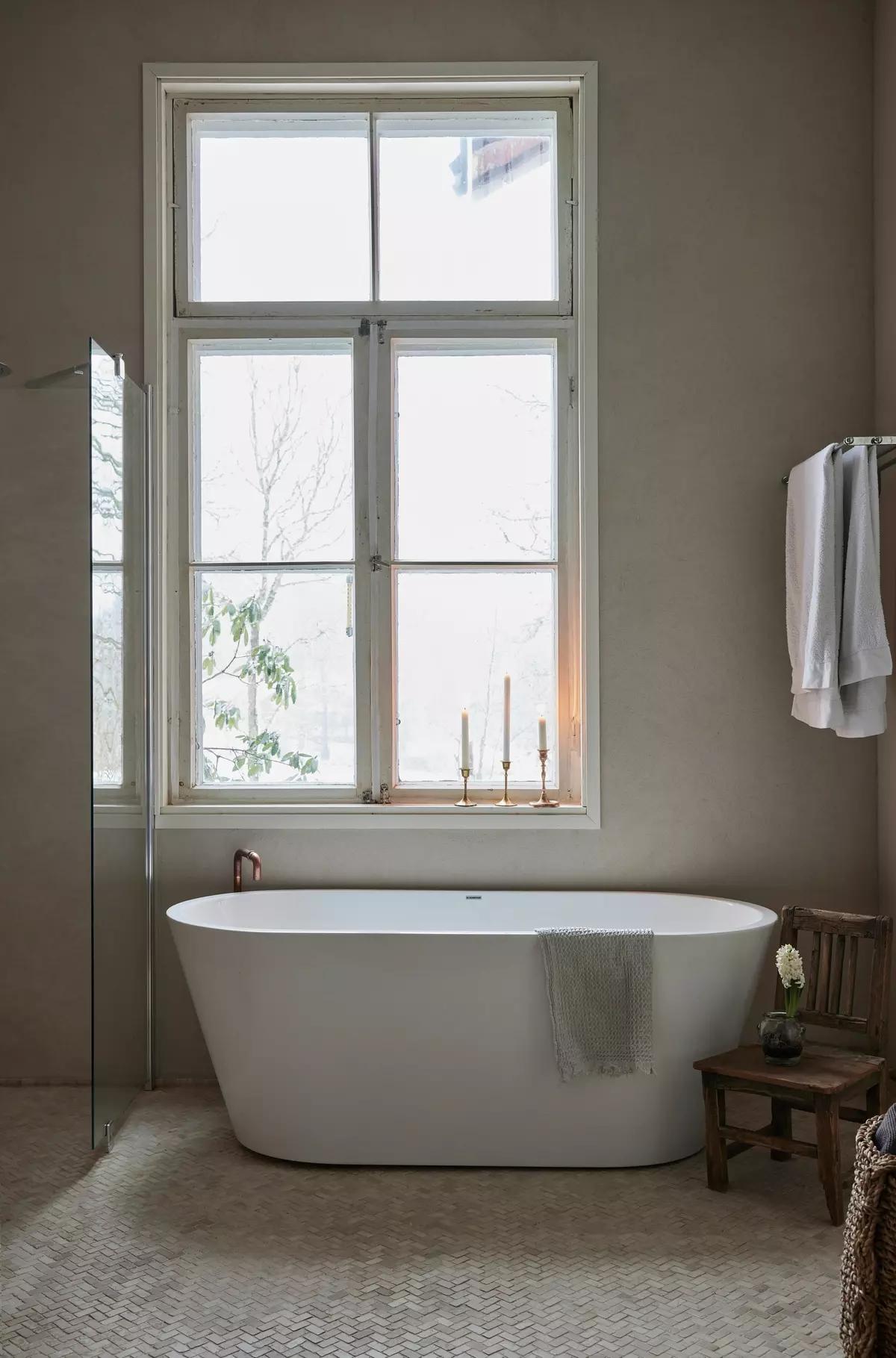 Bathroom with a deep white bathtub by a large window and candles on the windowsill
