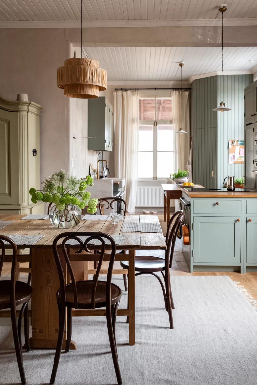 Spacious dining area with a wooden table, chairs, a vase of flowers and a view into the light-green kitchen