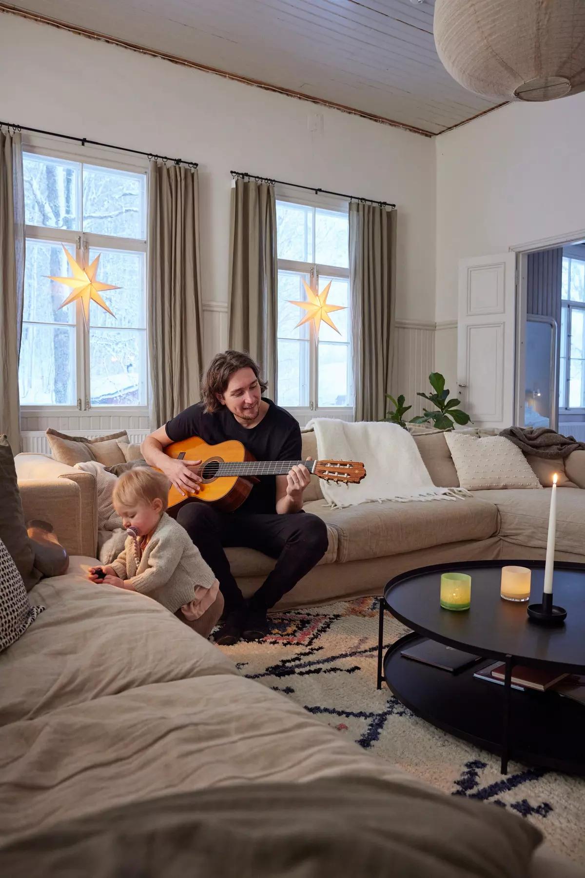 Man playing guitar for a child on the beige sofa, with stars in the windows and candles on the table