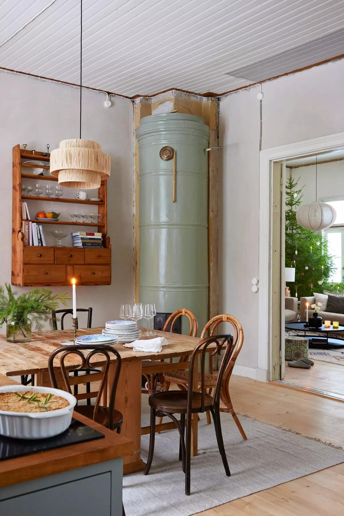 Dining table with chairs, a shelf of dishes, a green stove in the corner, and a view of the living room tree
