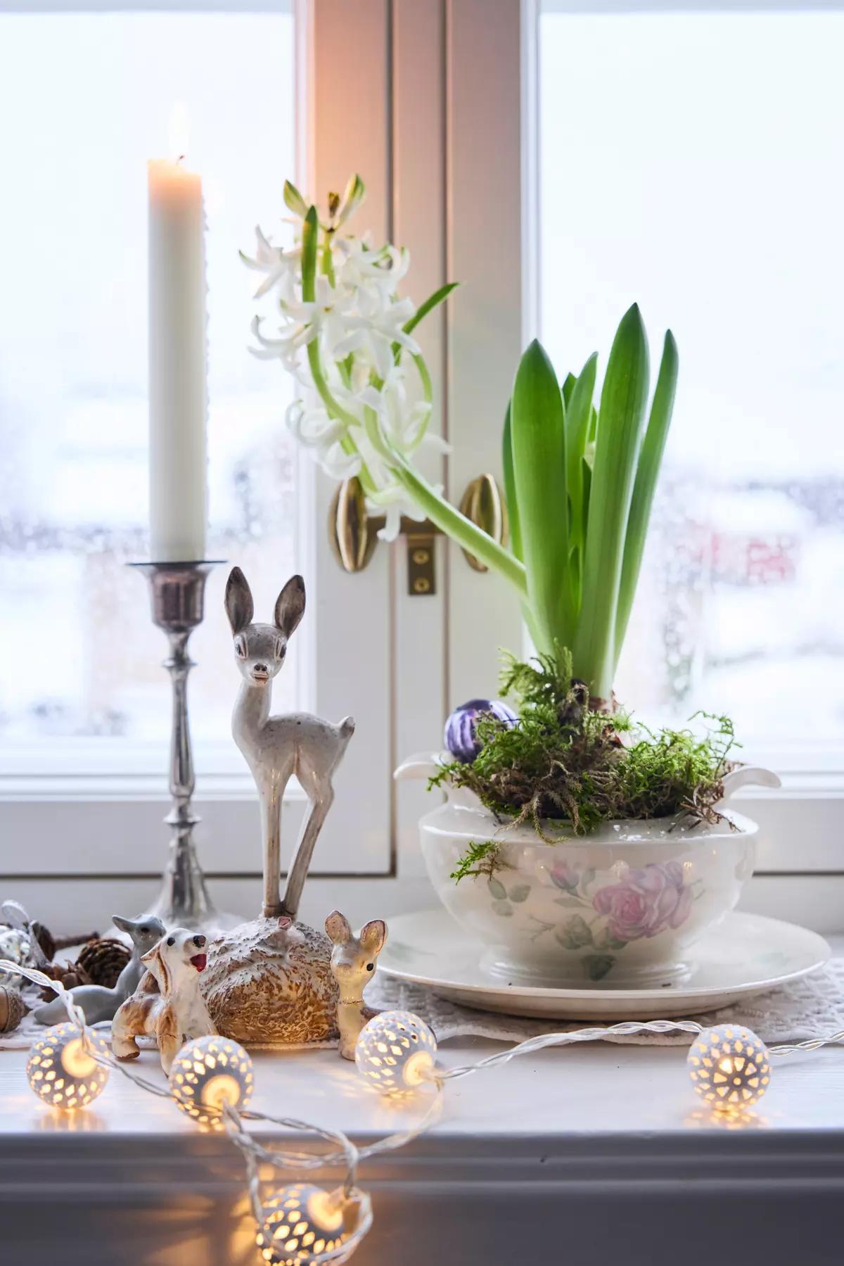 Festive windowsill display with Christmas figurines, a candle, a garland and a hyacinth in a vase