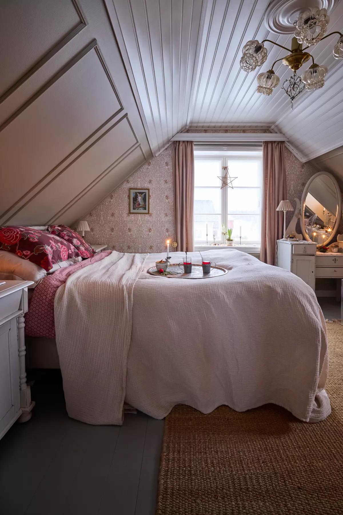 Cozy Scandinavian attic bedroom in soft pink tones, with a round tray holding drinks and a candle on the bed