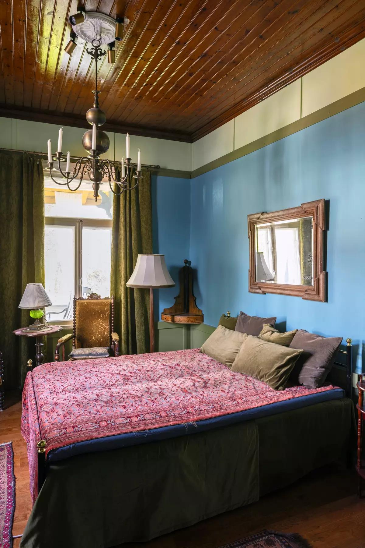 Bedroom with a wooden ceiling, blue walls, retro furniture and a mirror above the headboard